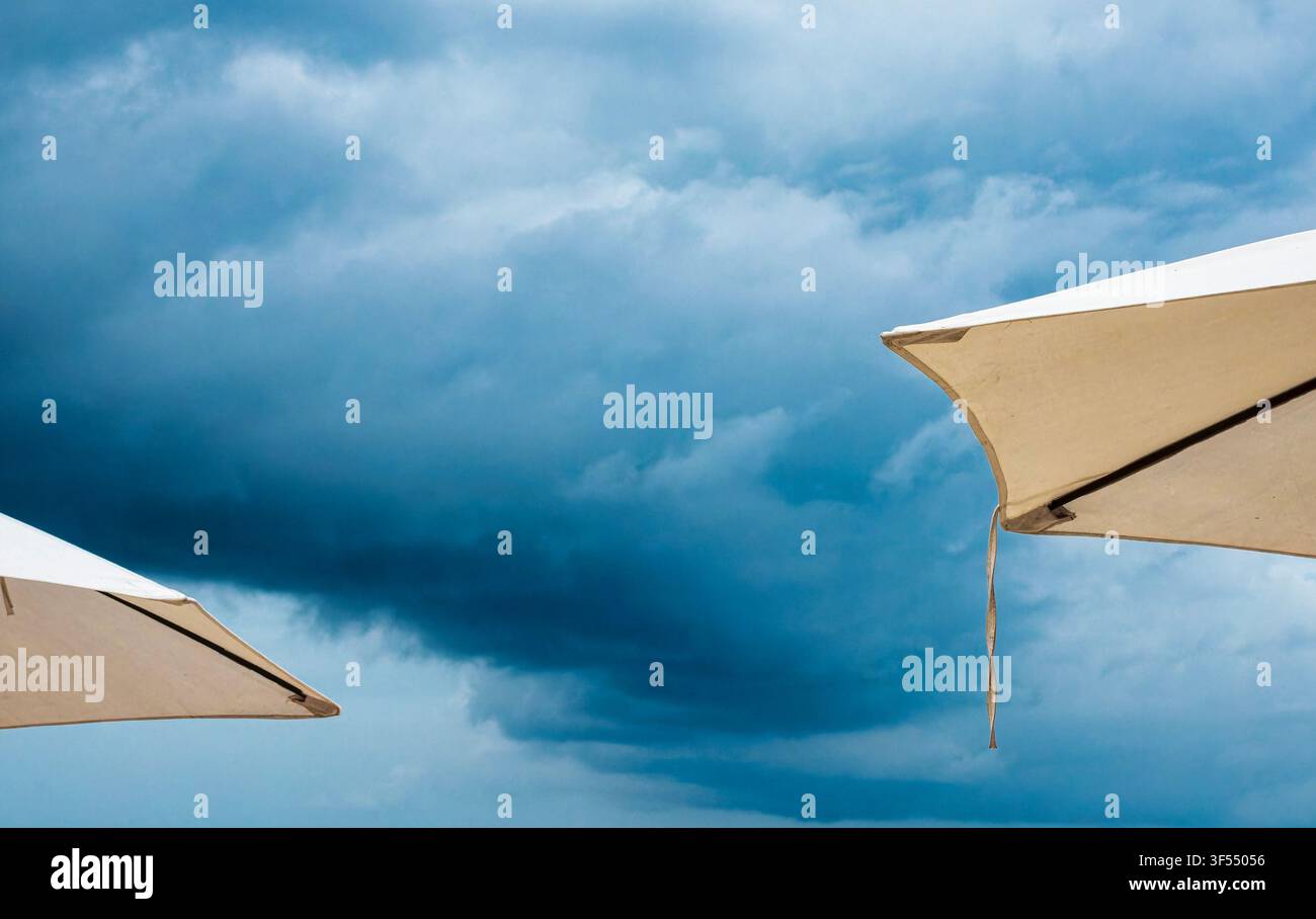 White beach umbrellas set against a dramatic, stormy sky. Stock Photo