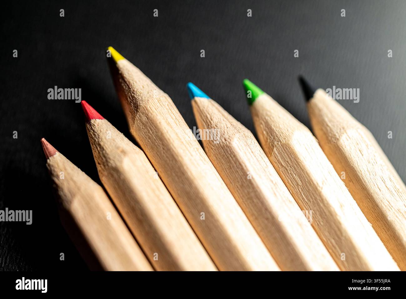 Close up macro shot of sharp wooden colored pencils lined up diagonally on a dark black background Stock Photo