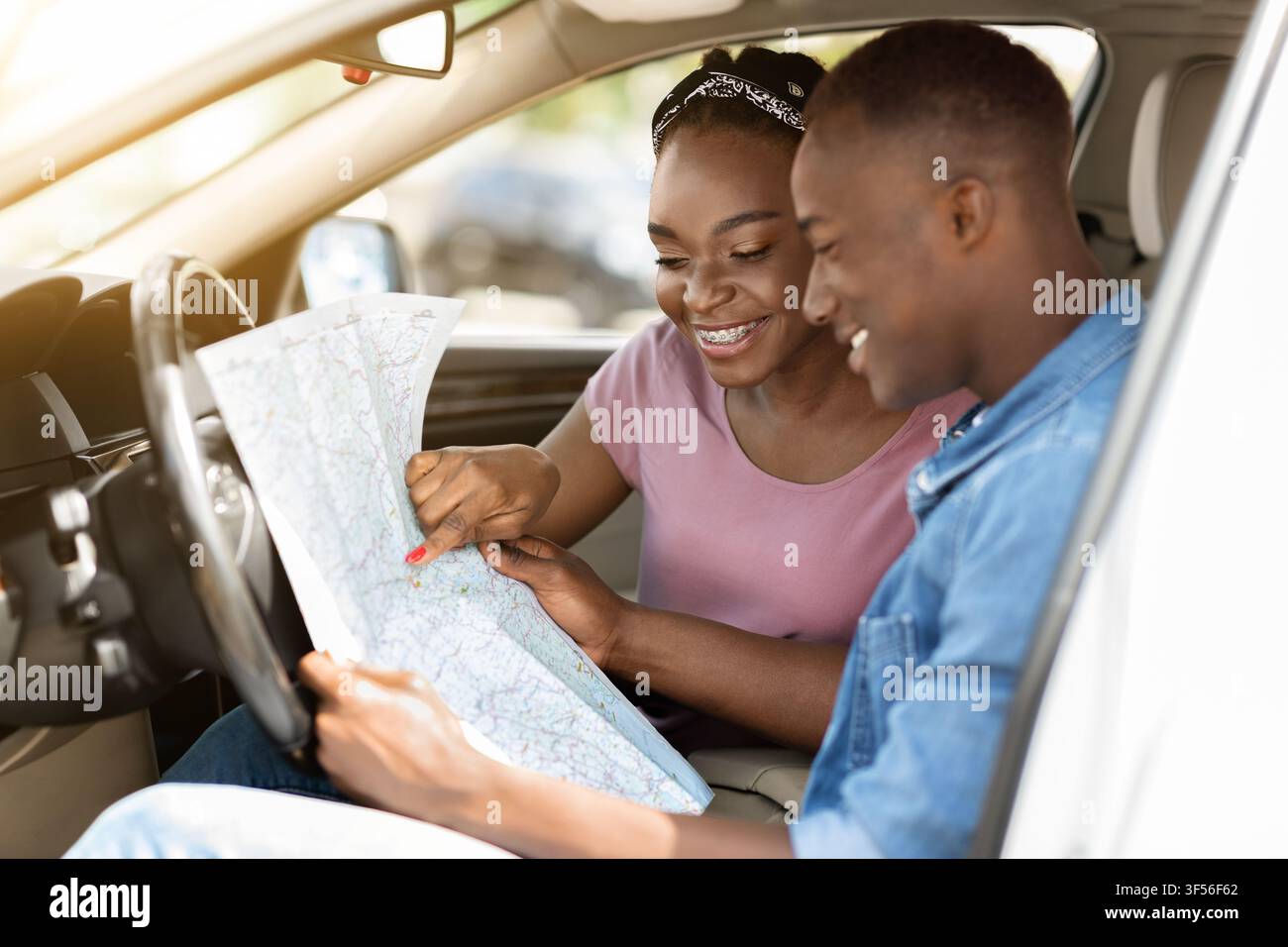Enthusiastic black couple reading map while having car trip Stock Photo