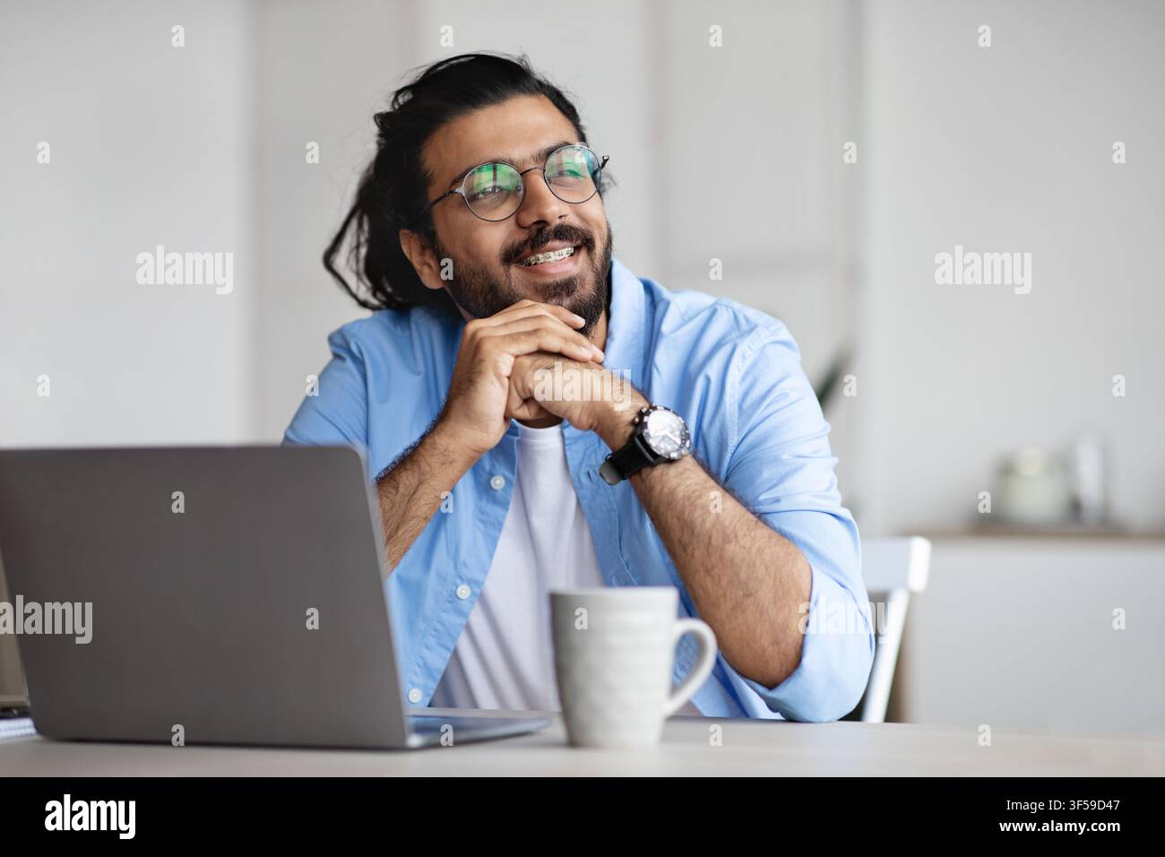 Pensive freelancer thinking about something while working on laptop at home office Stock Photo