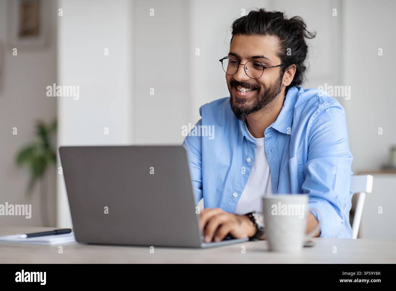 Smiling Indian Writer Using Laptop Computer, Sitting At Desk In Home Office Stock Photo