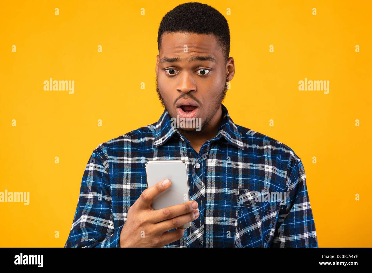 Shocked Guy Looking At Smartphone Reading Shocking News In Studio Stock Photo