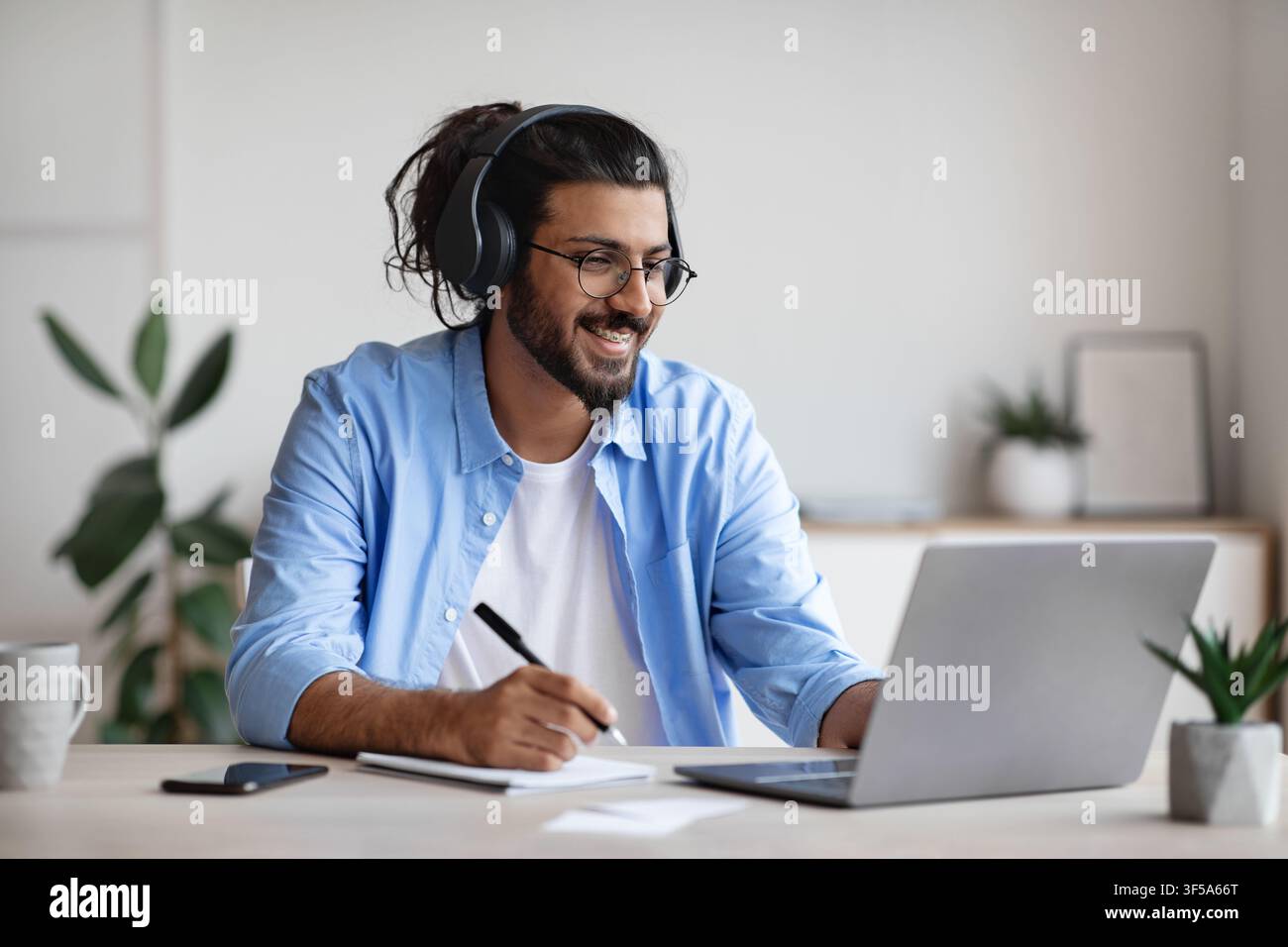 Distance Learning. Indian Guy Watching Webinar On Laptop Computer And Taking Notes Stock Photo