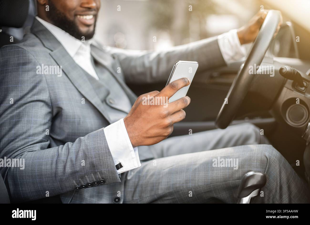 Black guy in suit using smartphone while driving Stock Photo