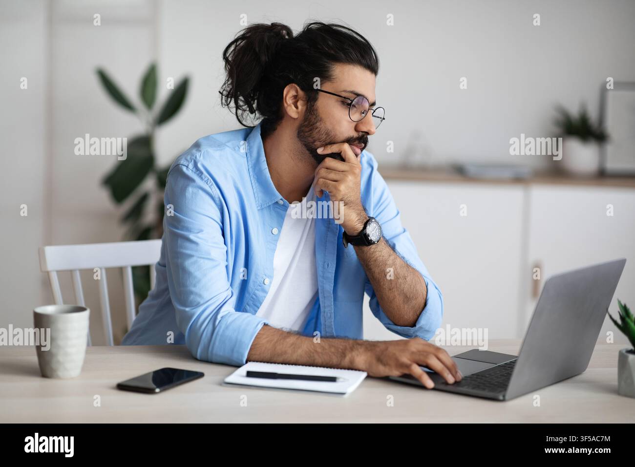 Thoughtful Indian Freelancer Working With Laptop At Home Office, Looking At Screen Stock Photo