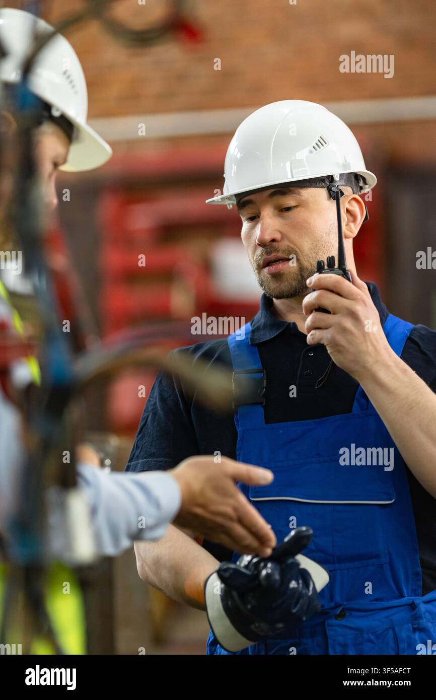 Industrial worker using two-way radio while discussing factory operations with supervisor Stock Photo