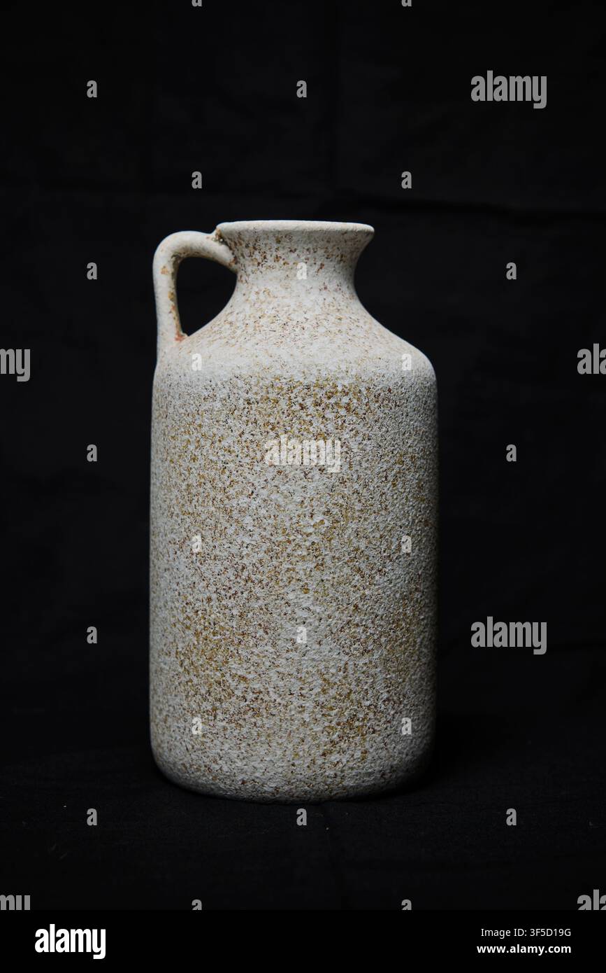 Rustic speckled ceramic jug with a handle on a dark background Stock Photo