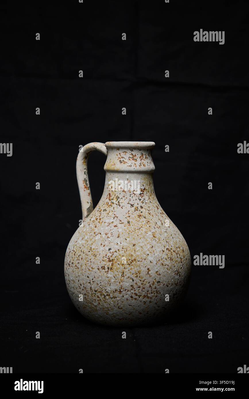 Rustic stoneware jug standing with textured speckled surface on a plain black background Stock Photo