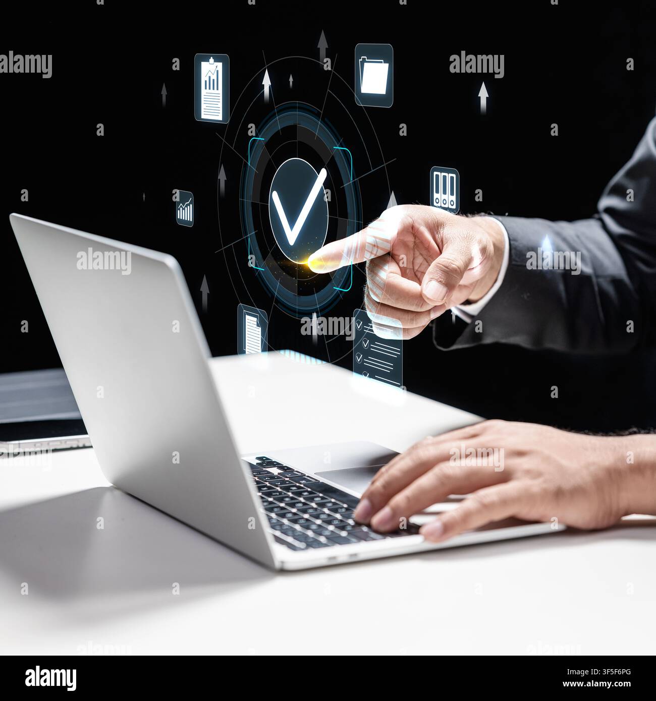 Businessman using a laptop while interacting with a digital holographic interface featuring a checkmark, symbolizing data verification, security, qual Stock Photo