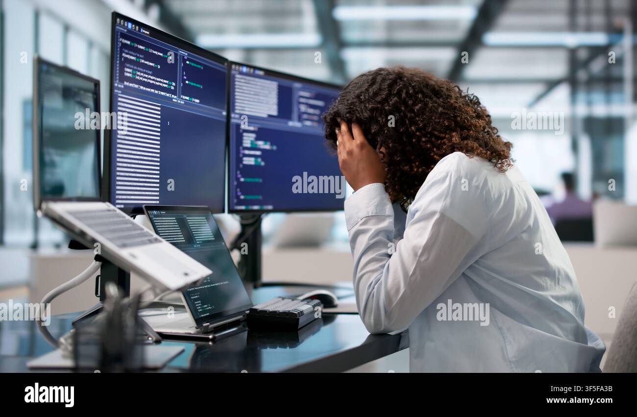 Tired African Software Engineer Rubs Head While Coding Late At Desk. Stock Photo