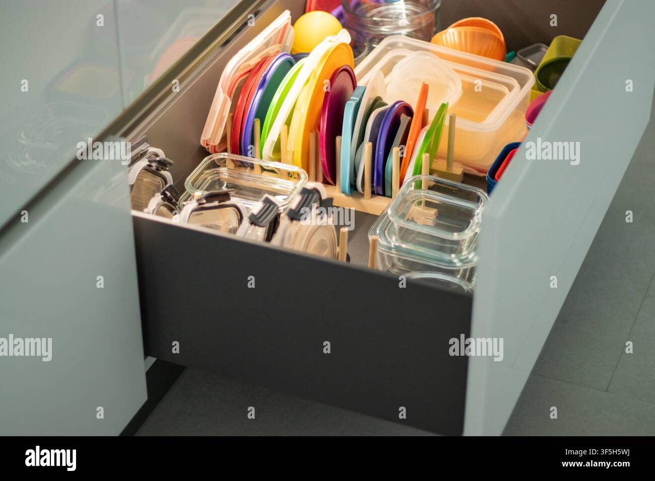 Kitchen drawer filled with colorful plastic lids, glass containers, and various kitchen storage items organized neatly Stock Photo