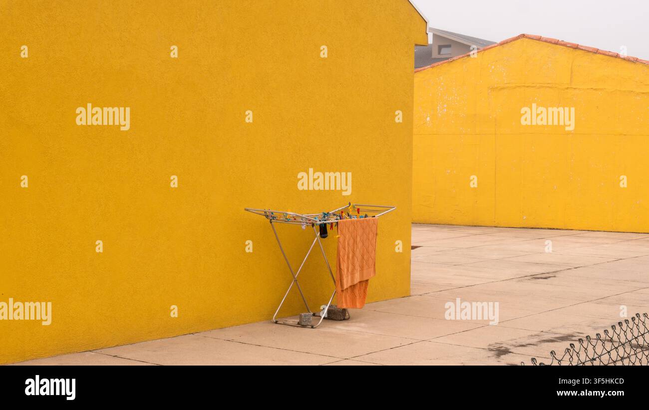 Orange Towel Drying on a Folding Rack Against a Bright Yellow Rendered Wall — Concept: Minimalist Colour Block Composition, Everyday Domestic Life Stock Photo