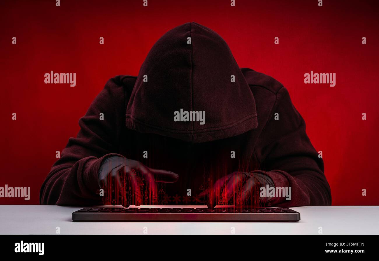 Anonymous hacker in dark hoodie using keyboard computer with digital code overlay on red. Cyberattack, hacking, cybersecurity threat, ransomware, data Stock Photo
