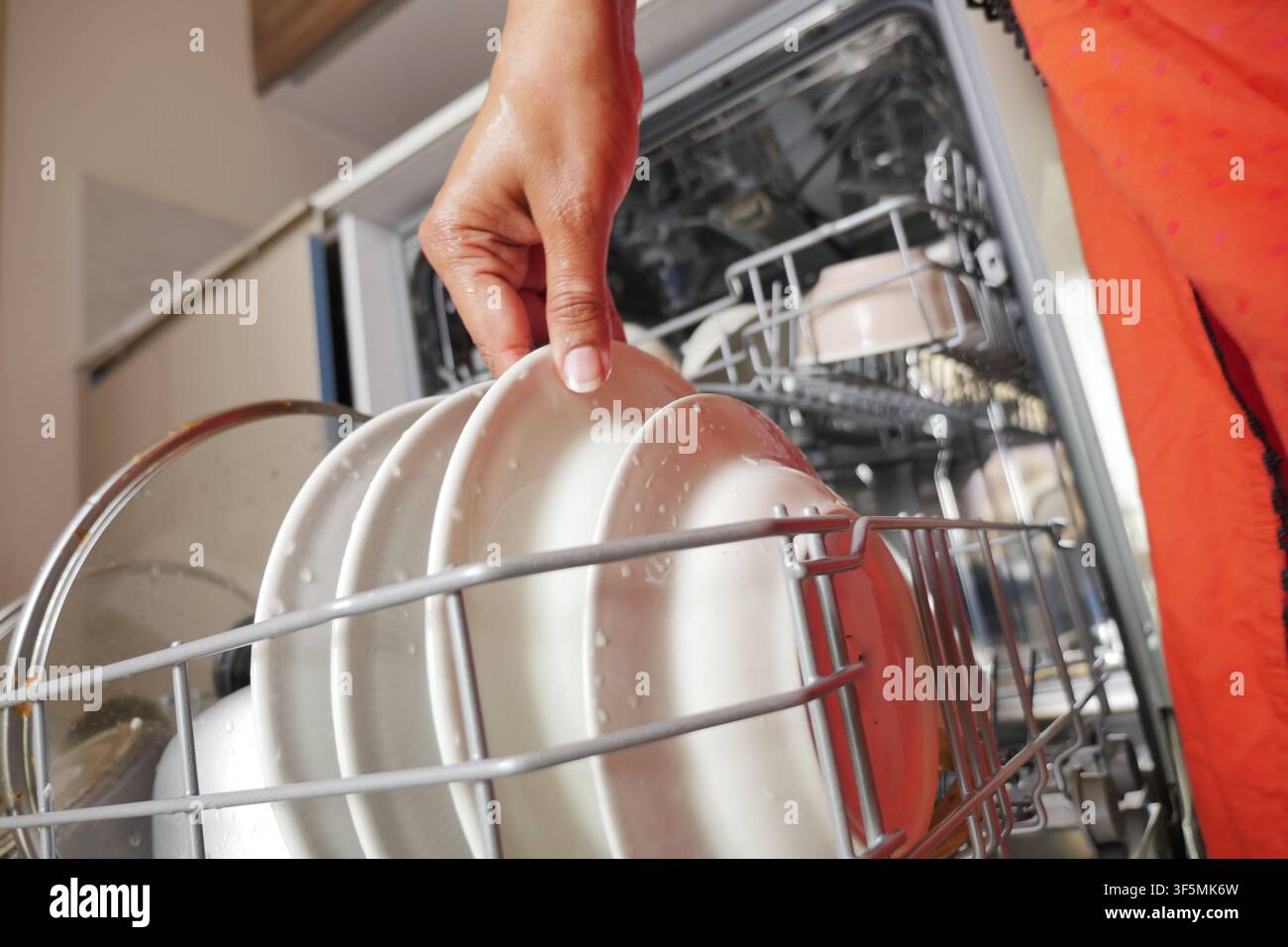 Hand places plates in dishwasher Stock Photo