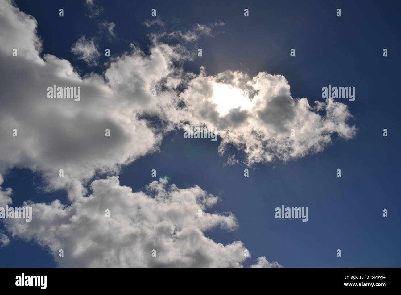 Sunlight breaking through silver-lined cumulus clouds in a deep blue sky Stock Photo