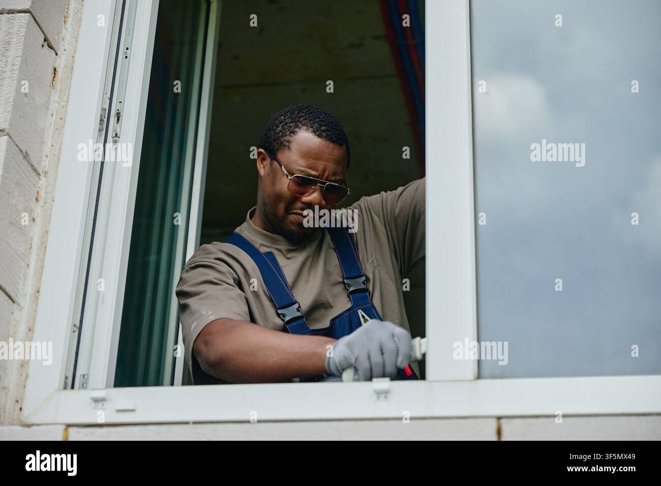Black Man Fixing Window Frame with Tool during House Renovation Stock Photo