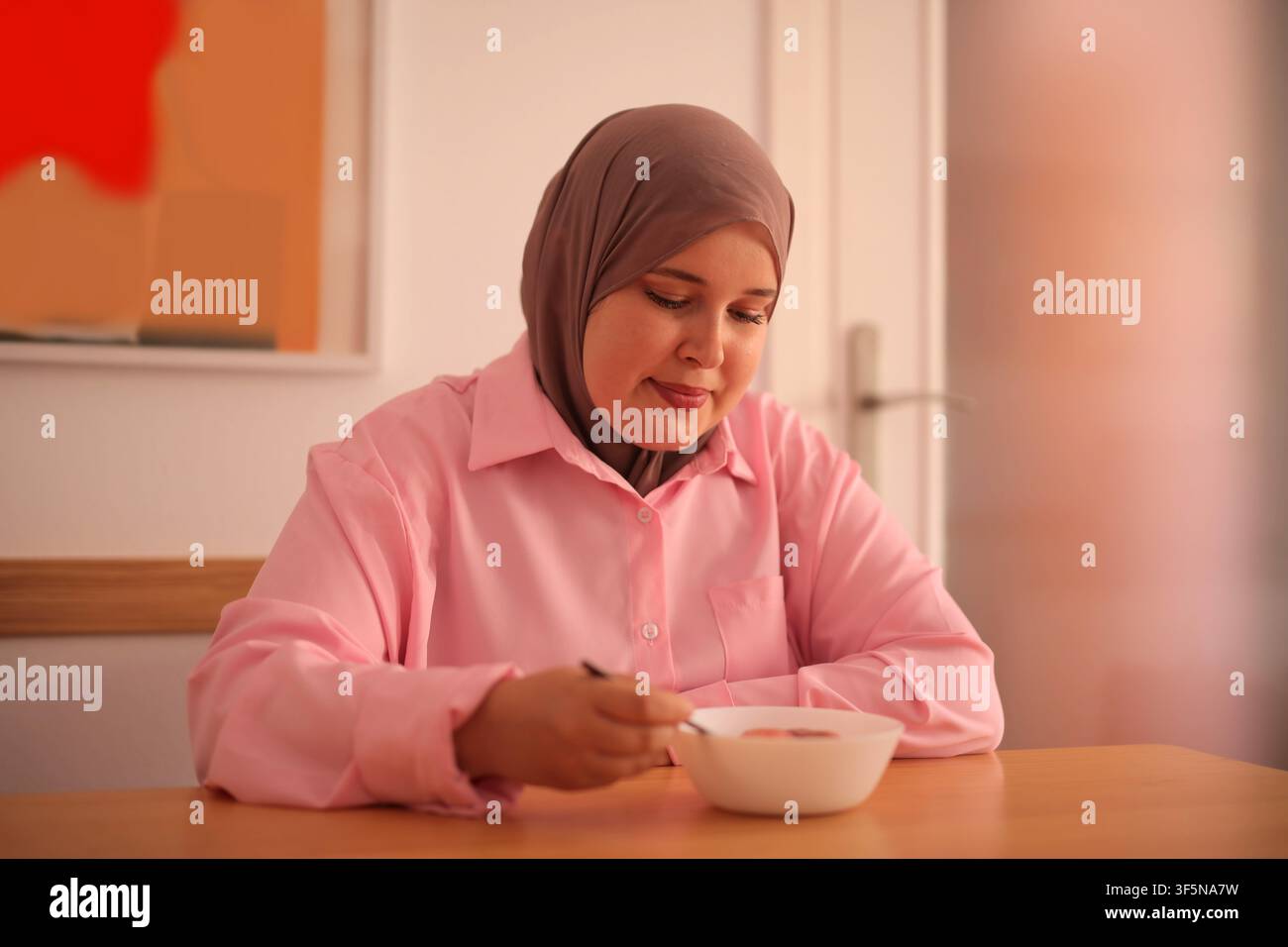 Smiling woman wearing a hijab eats her breakfast Stock Photo