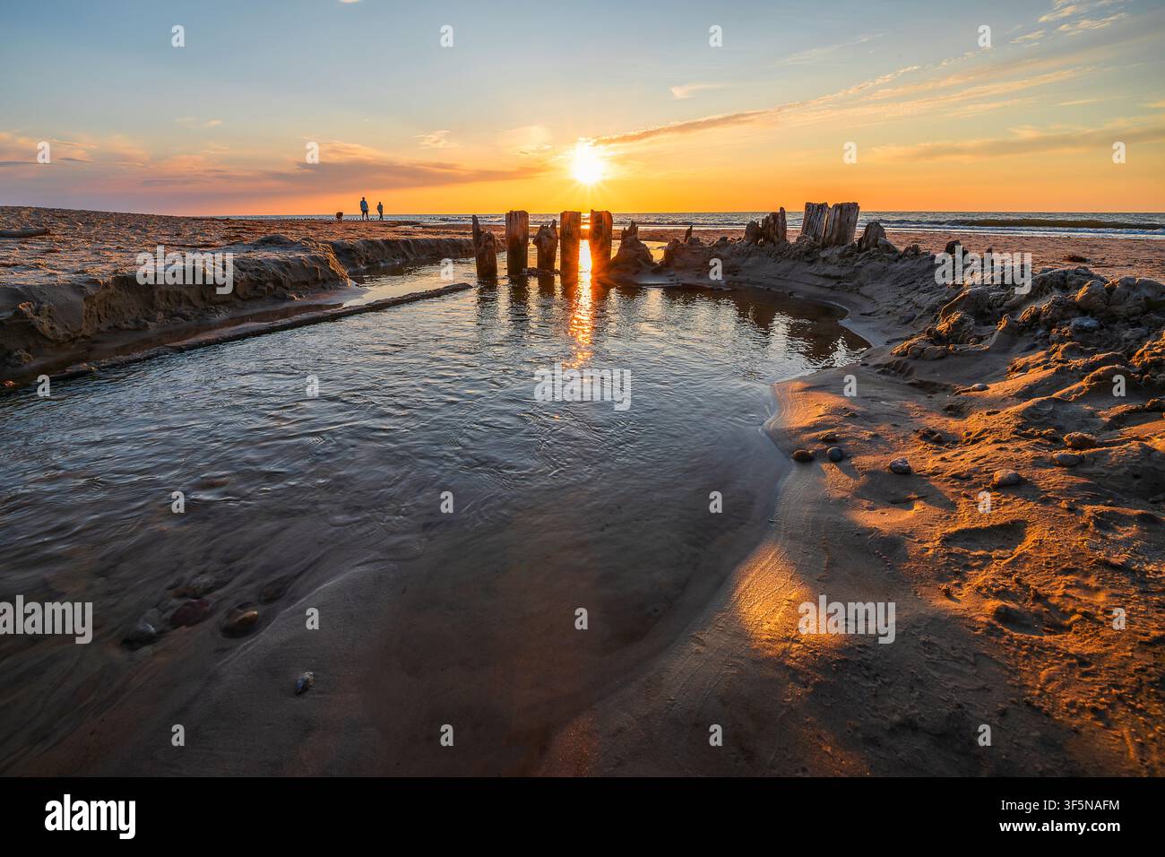 Small stream flowing into sea on beach at sunset Stock Photo