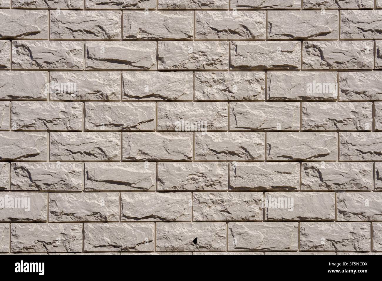 Light gray stone wall with decorative rectangular bricks and deep relief textures. Modern cladding material with rough split surfaces for a clean arch Stock Photo