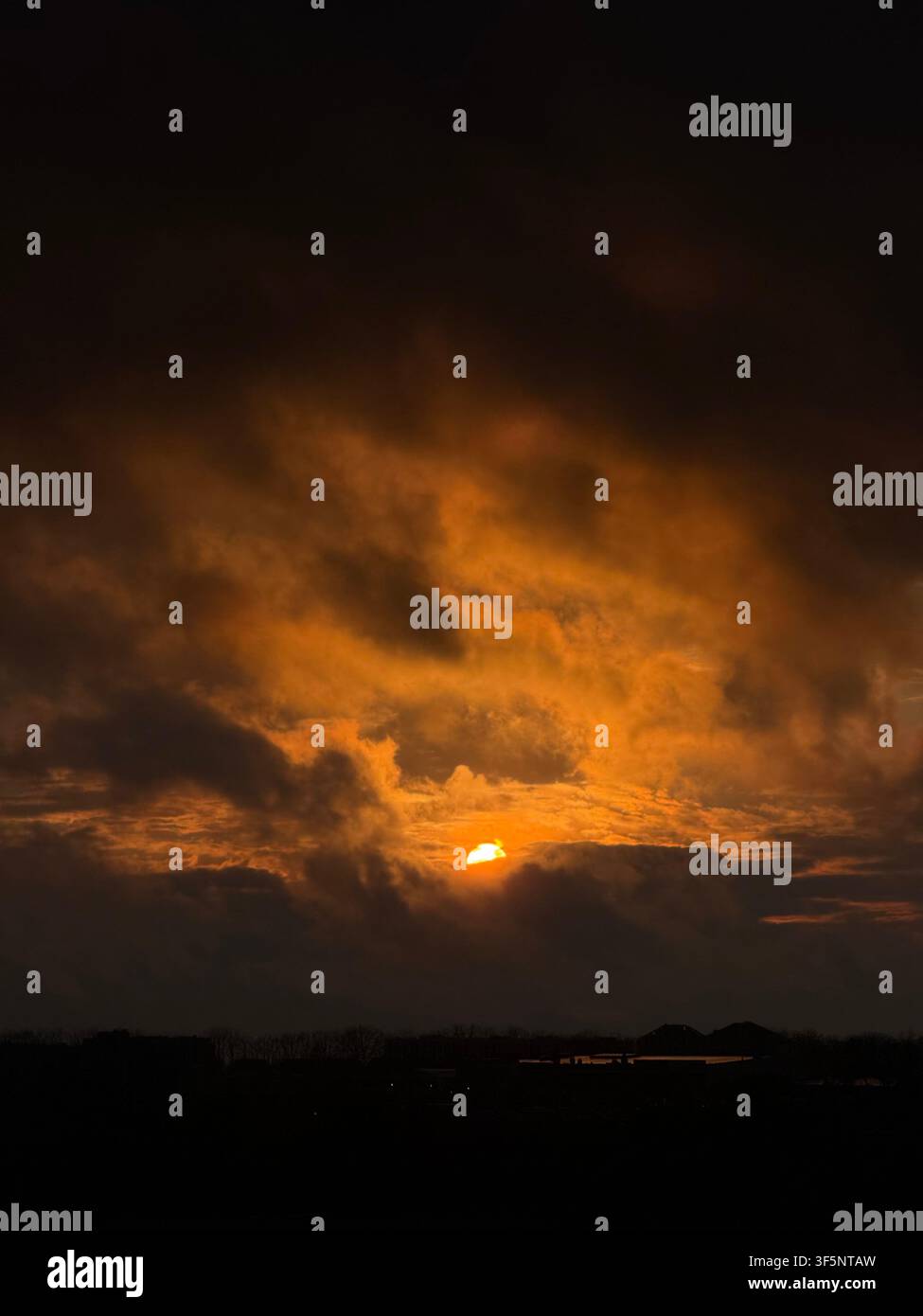 Dramatic orange sunset glowing through dark clouds over the horizon Stock Photo
