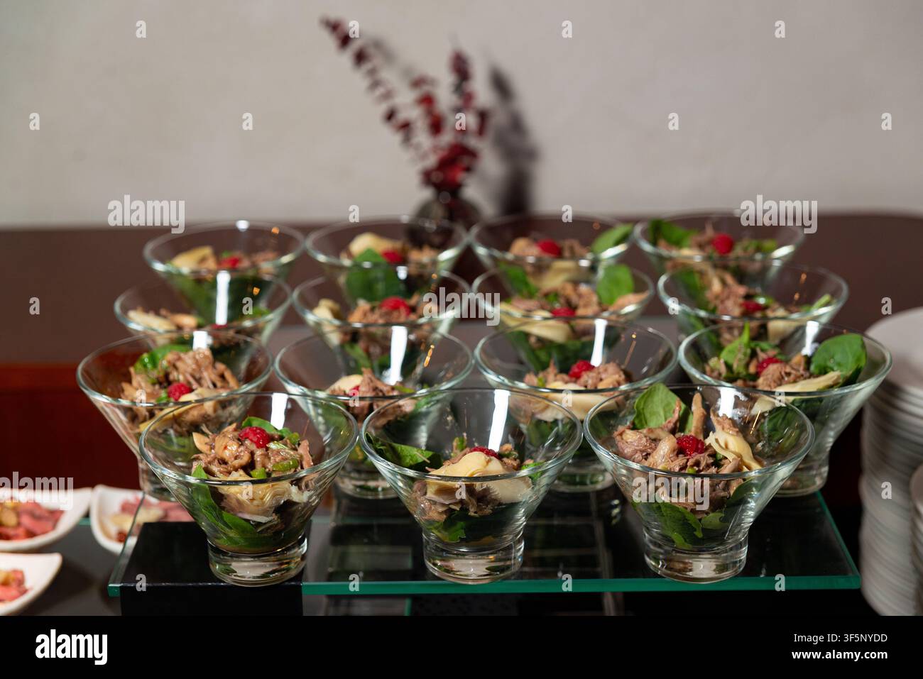 An array of individual salad servings is elegantly presented in glass cups on a buffet table. Each cup contains a mixture of greens, shredded meat, ch Stock Photo