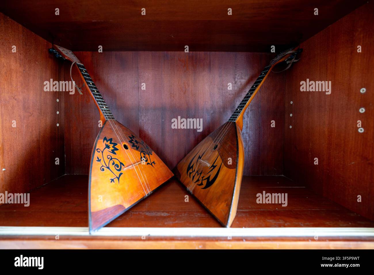 Two traditional folk string instruments stored in a wooden cabinet with intricate patterns painted on the triangular bodies, reflecting heritage and a Stock Photo