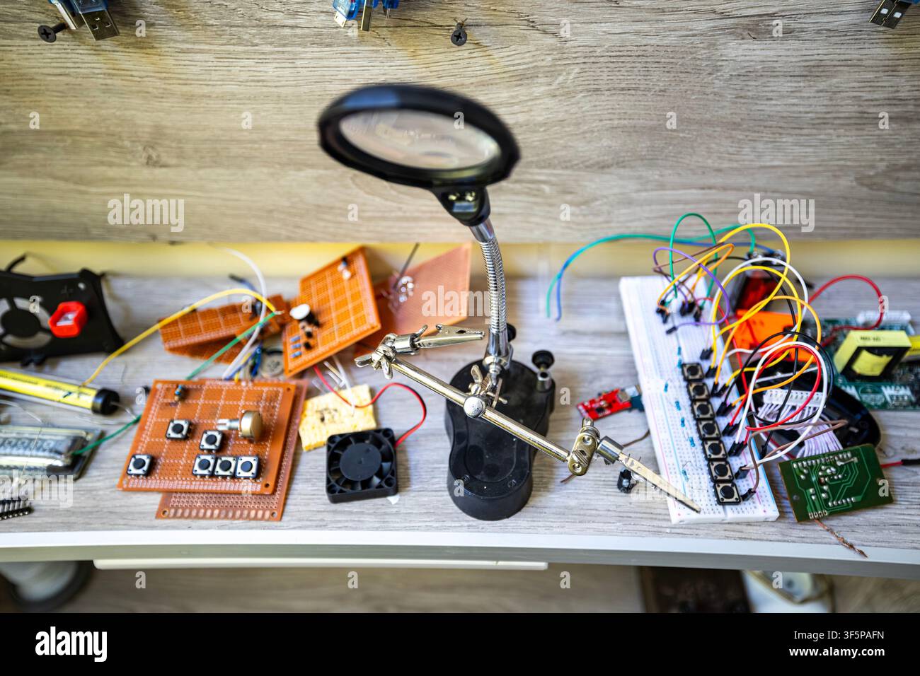 Electronic components and tools on a cluttered workbench for technical hobby projects a magnifying lamp with helping hands, scattered circuit boards, Stock Photo