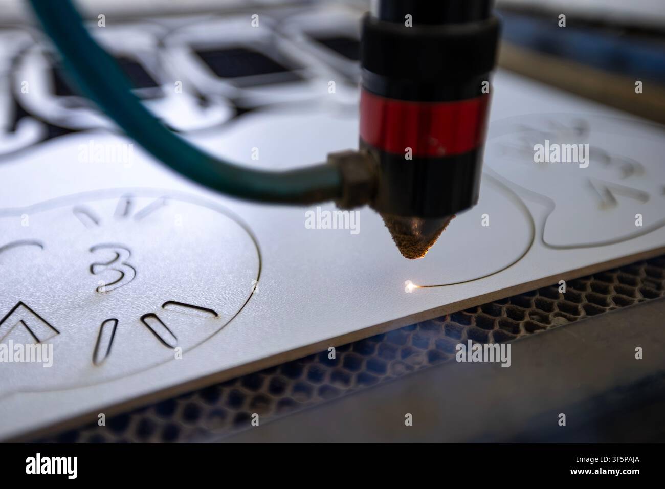 CNC laser cutting machine creates precise patterns on a flat white material sheet using a focused beam, automated industrial technology process, metal Stock Photo