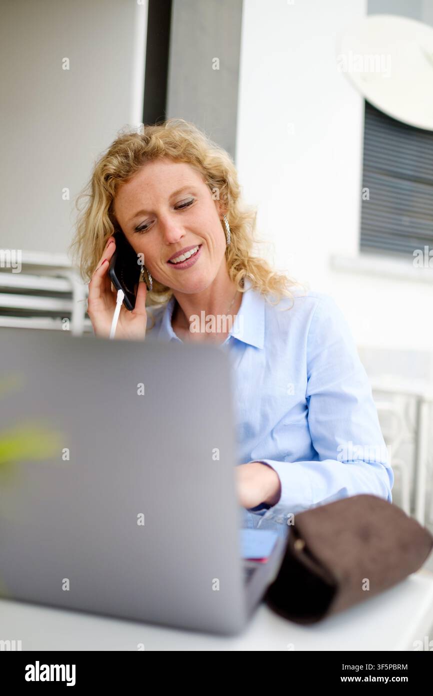 Woman using laptop and smartphone for remote work outdoors Stock Photo