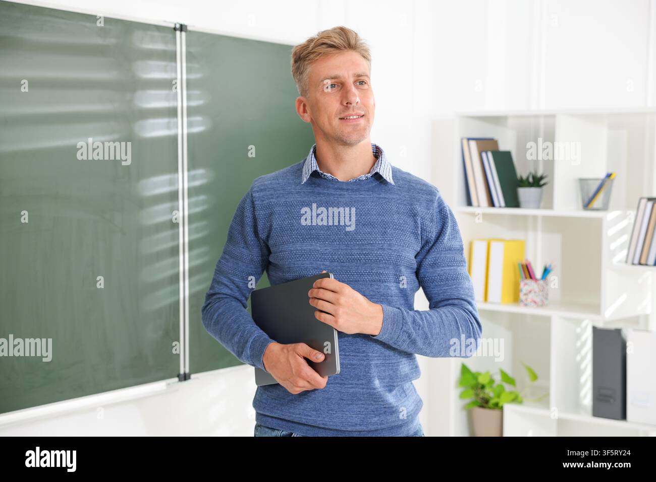 Smiling teacher with laptop near chalkboard in classroom Stock Photo
