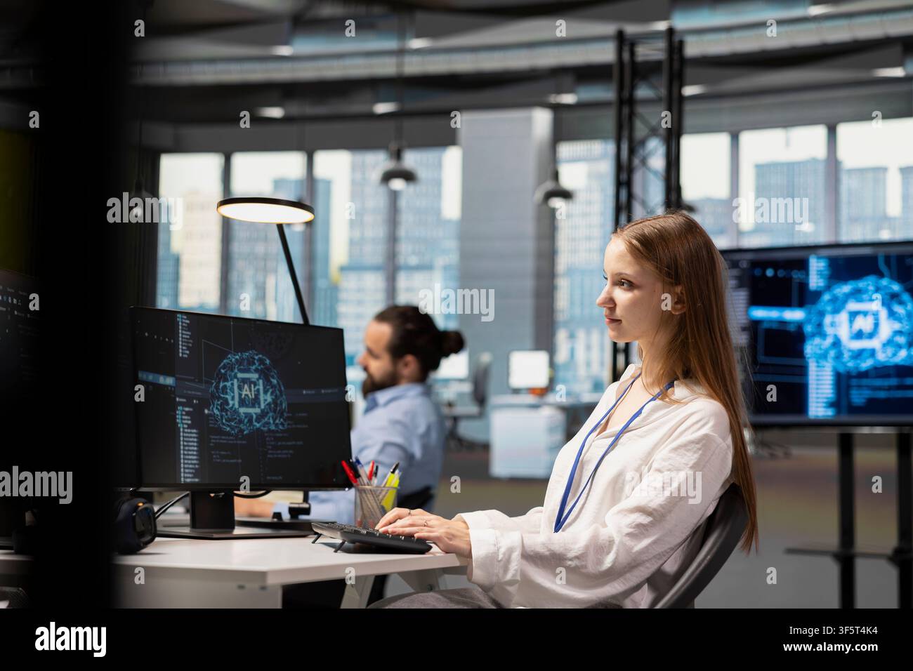 Female developer in modern office leveraging AI tools to automate routine coding tasks. Young programmer using artificial intelligence to accelerate software feature development Stock Photo