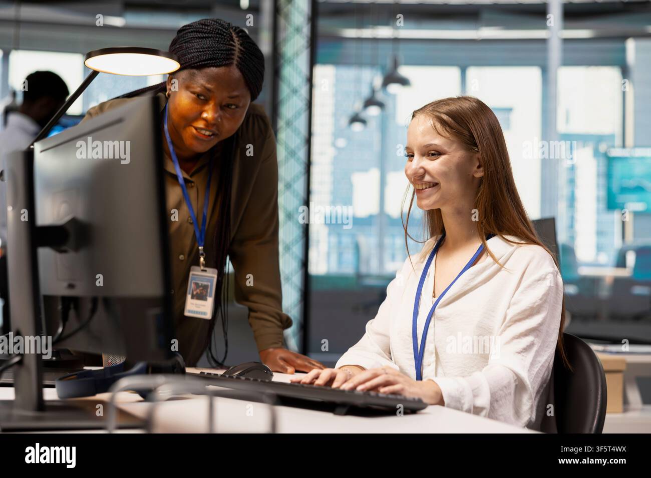 Friendly IT team leader teaching young software developer to use artificial intelligence. Joyous supervisor guiding junior dev through AI tool integration, mentoring her on using deep learning APIs Stock Photo