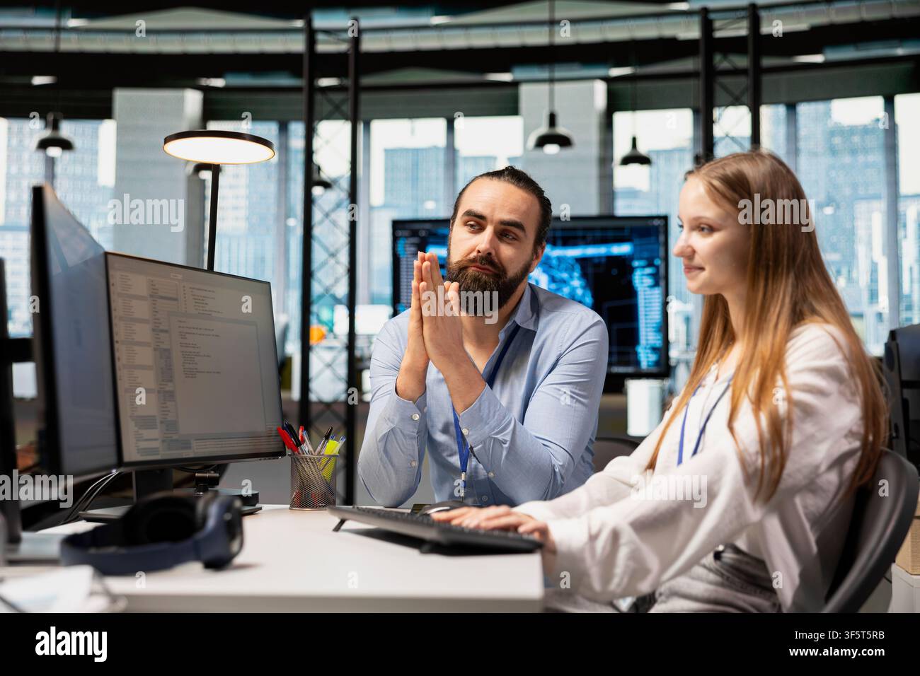 IT specialist helping young trainee coding during internship in tech startup. Lead system administrator providing support to new worker using PC in software development agency Stock Photo