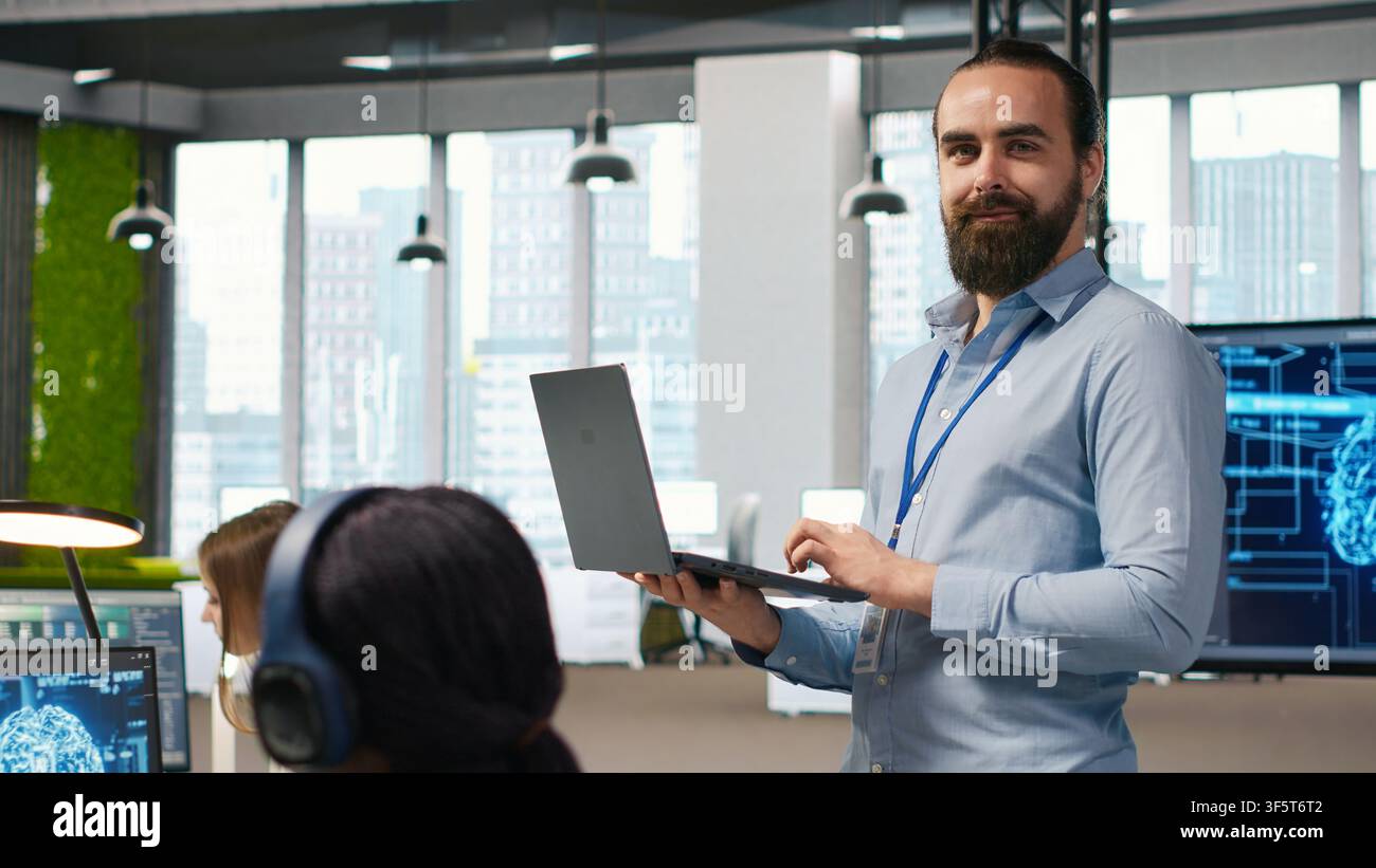 Jolly programmer coding AI algorithms on laptop to debug software issues and improving system stability. Smiling employee in tech startup office configuring settings using notebook, camera A Stock Photo