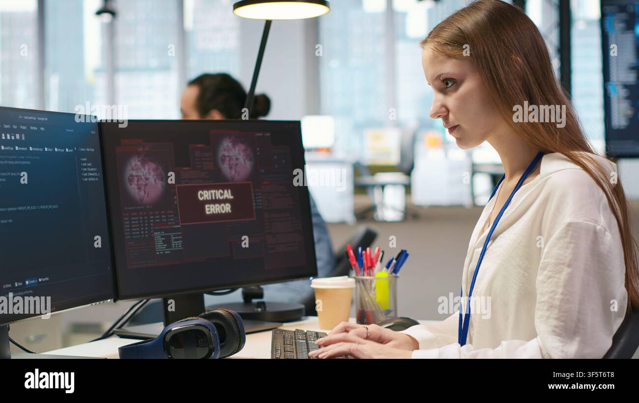 Female programmer in startup office struggling to fix application errors while coding. Young woman dealing with computer bugs while coding in software development agency, camera A Stock Photo