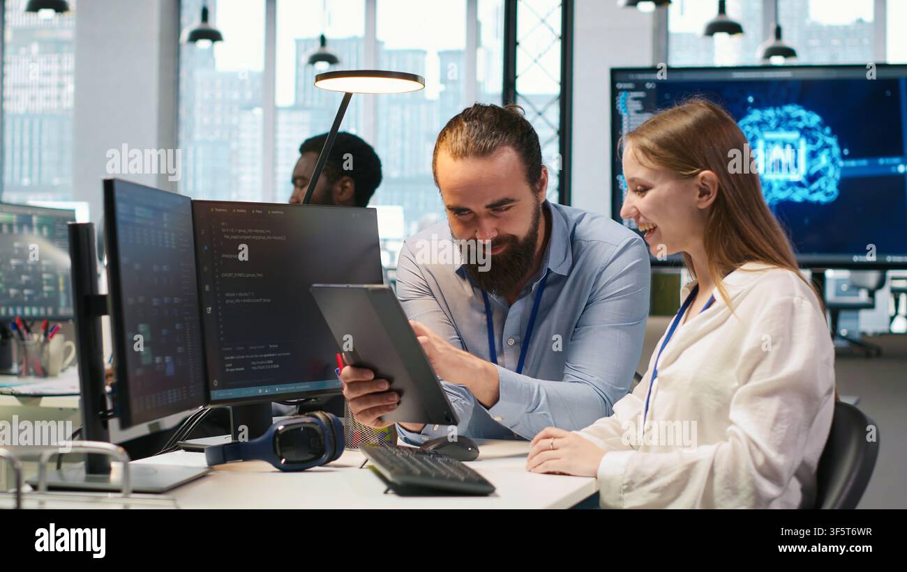Friendly team leader helping happy young engineer code AI algorithms to debug software issues and improving system stability. Helpful manager assisting smiling intern in tech startup office, camera A Stock Photo