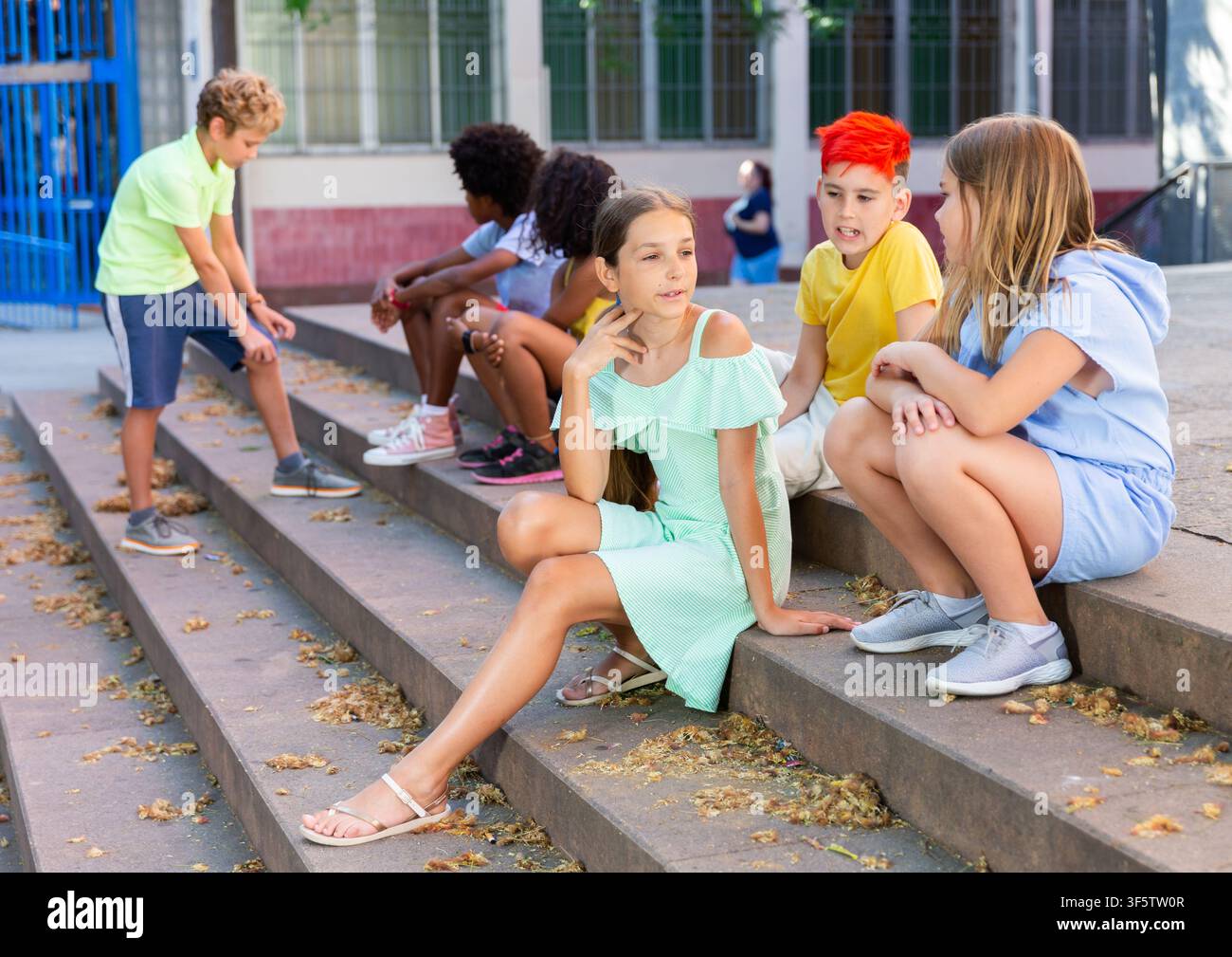 Happy tweenagers friends sitting on steps outdoors and chatting Stock Photo