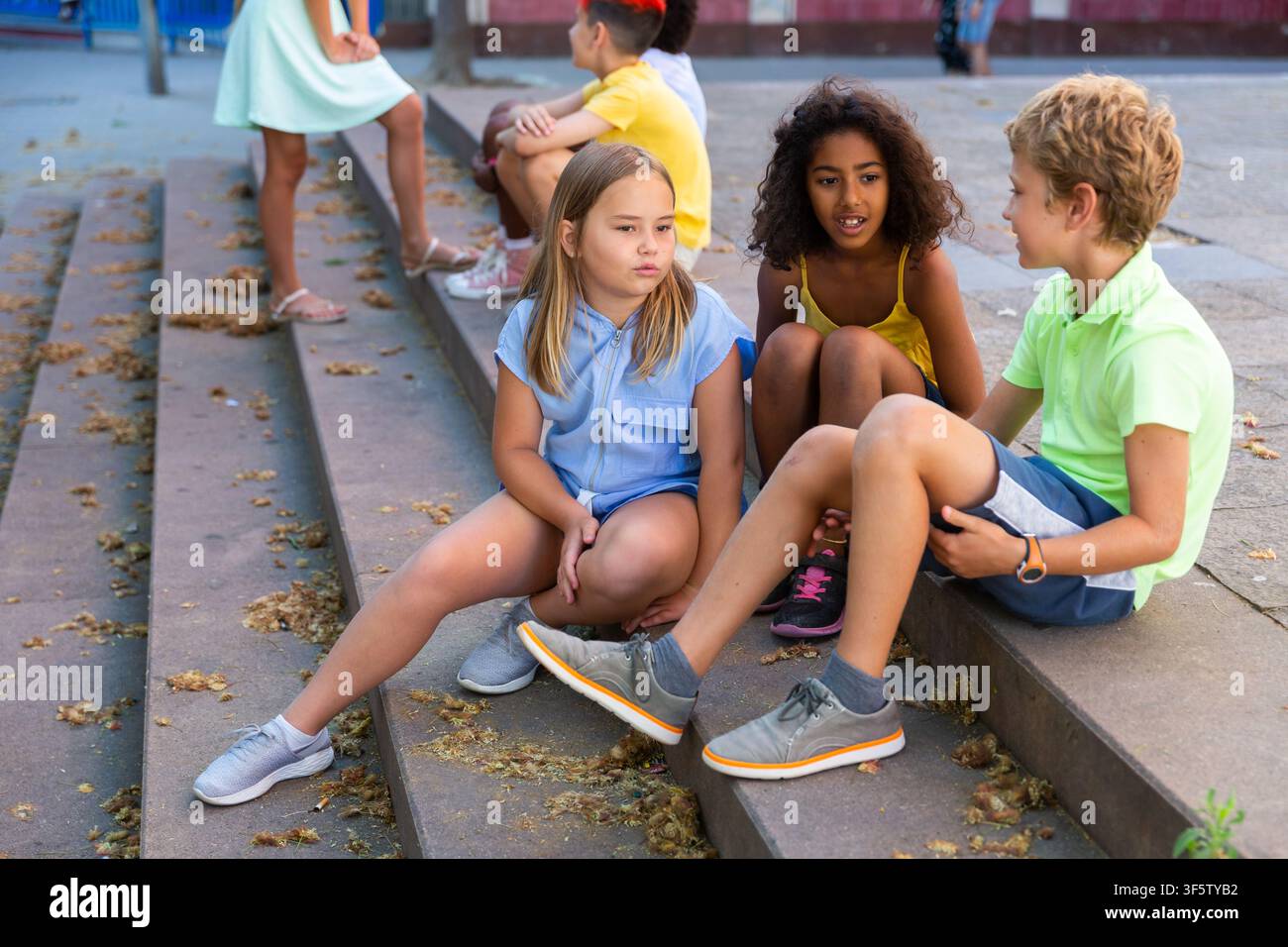 Happy tweenagers friends sitting on steps outdoors and chatting Stock Photo