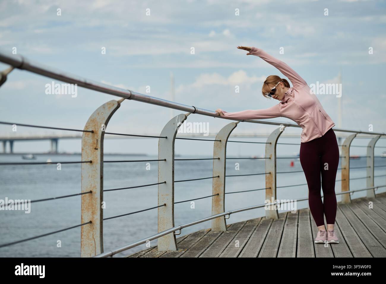 Woman Doing Side Bend Stretch on Waterfront Boardwalk Stock Photo