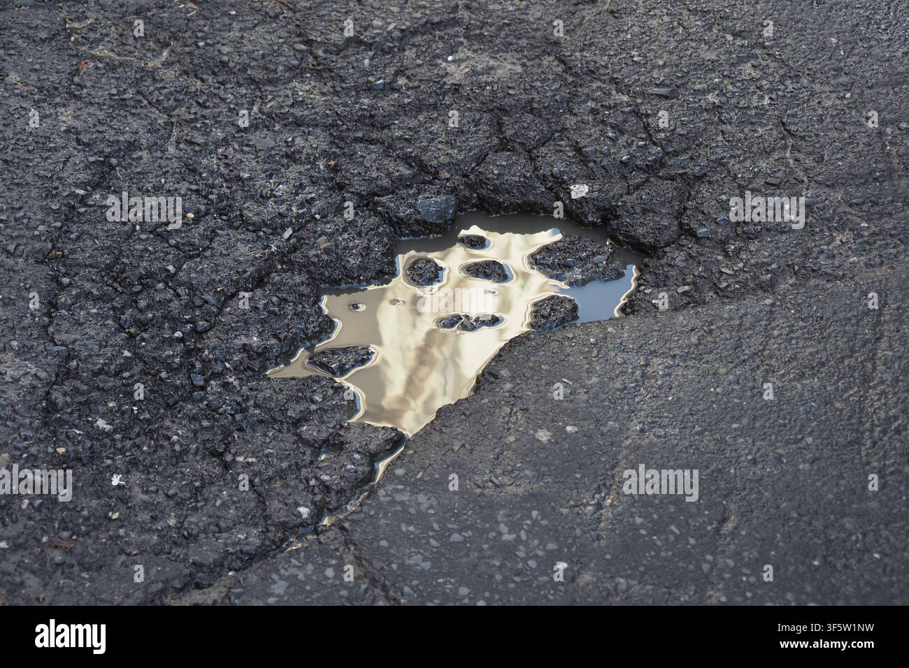 Water reflects on a cracked street surface Stock Photo