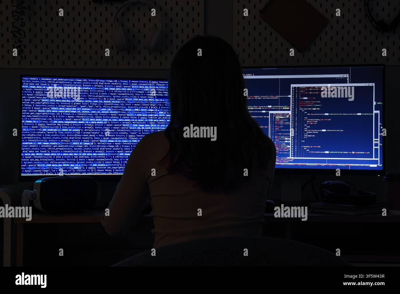Female programmer working on computer code at night, cybersecurity and software development concept, dark room environment Stock Photo