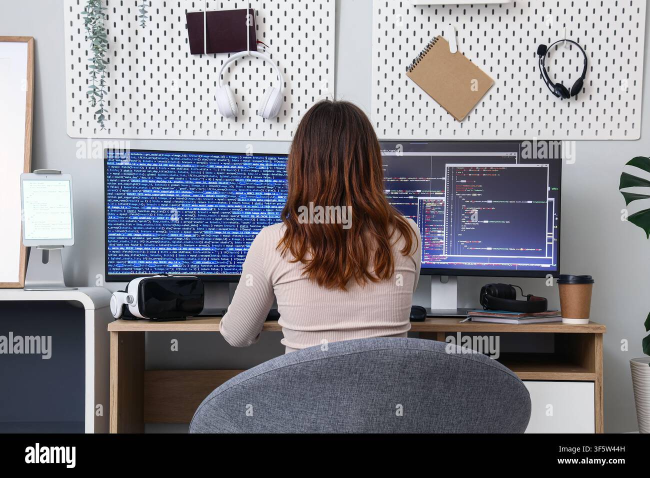 Female programmer coding on a desktop computer with multiple screens, Software development and IT career Stock Photo