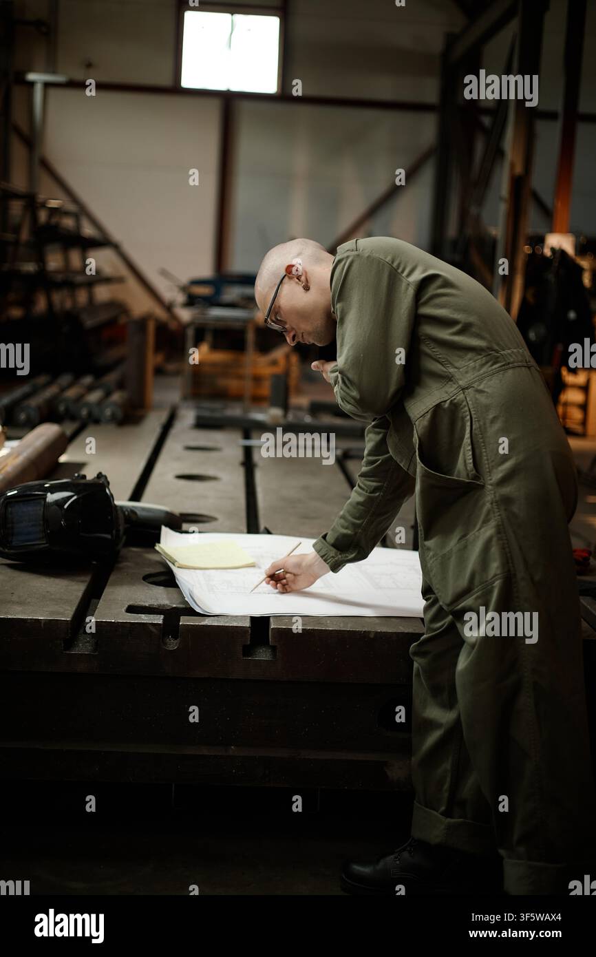 Male Welder Examining Blueprint in Metal Workshop Stock Photo