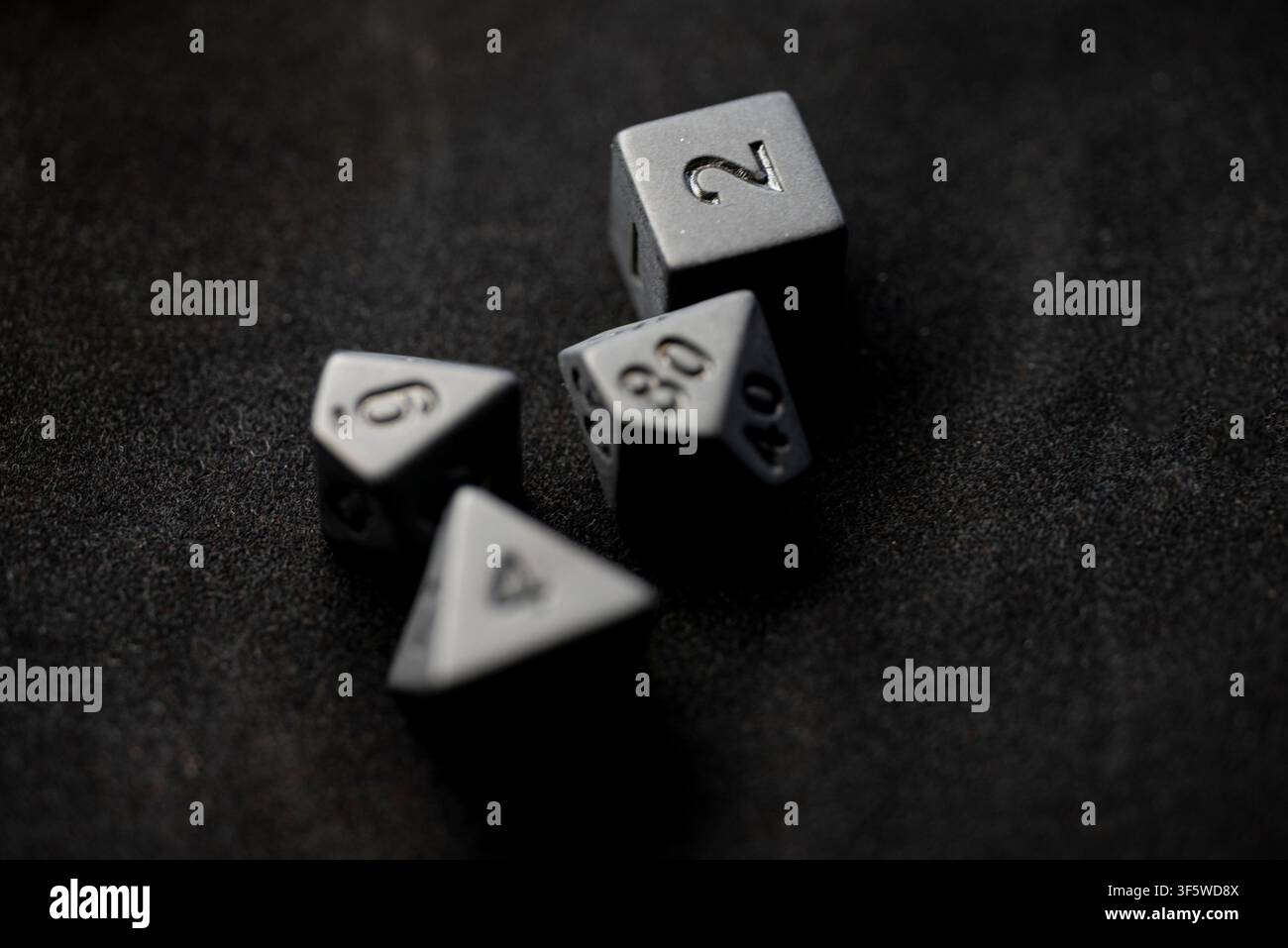 Strategic board game concept featuring dark metal multi sided dice scattered on dark fabric Stock Photo