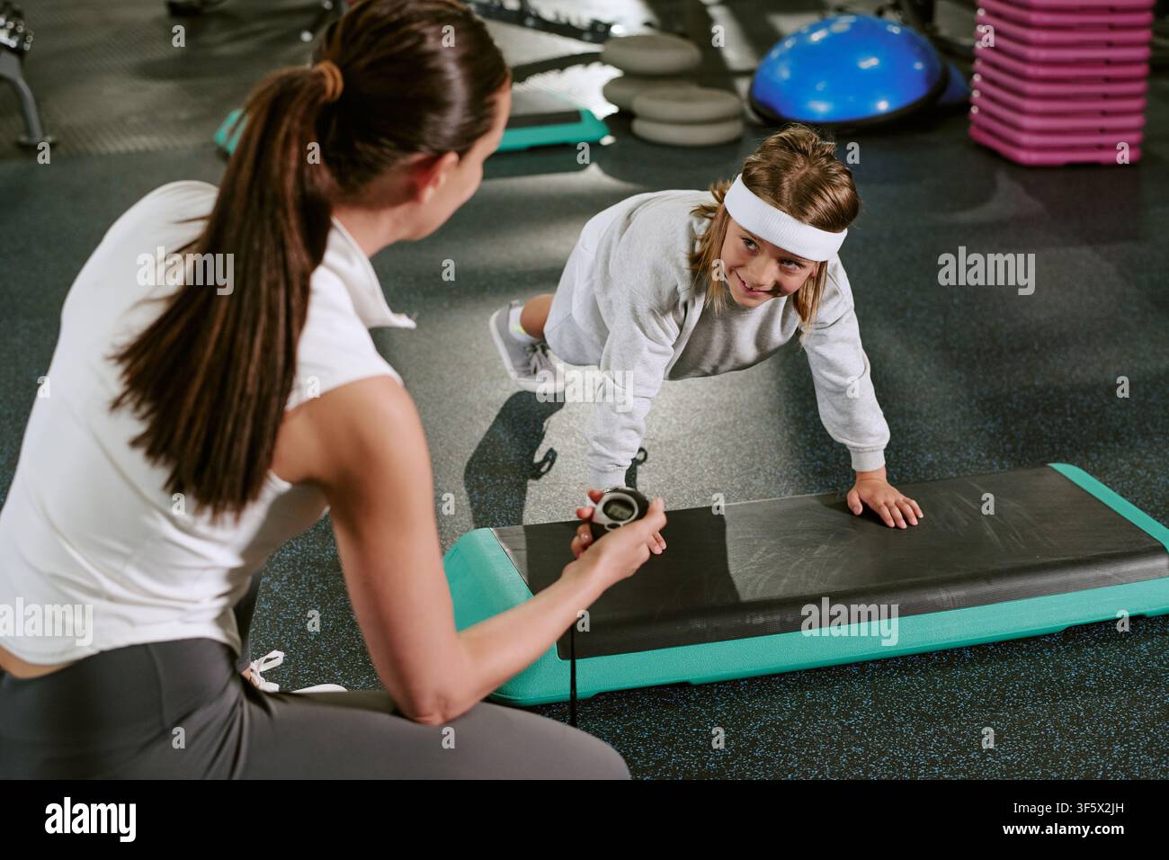 Female Trainer Timing Child Doing Plank Exercise in Gym Stock Photo