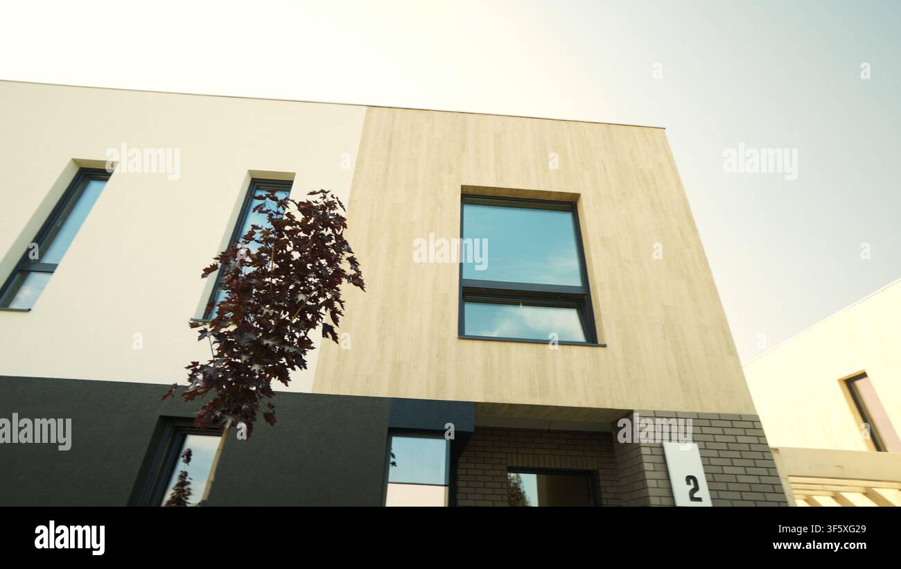 Modern townhouse exterior featuring minimalist architecture, contemporary design elements, and a small tree against a clear sky Stock Photo