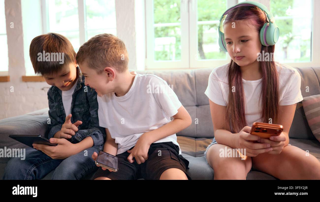 Three school-age friends using smartphones together while sitting on sofa Stock Photo