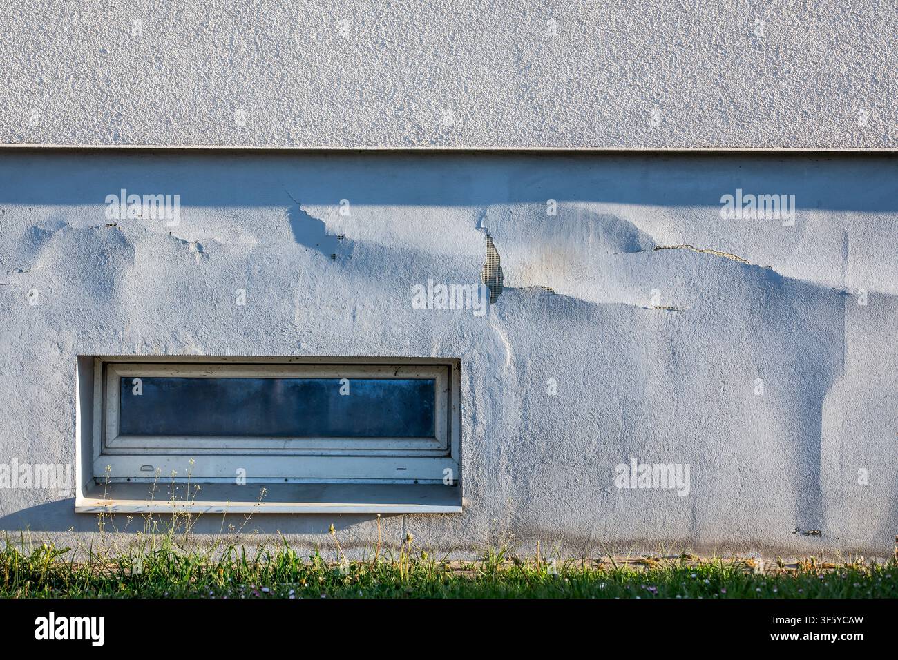 Old Building Wall With Peeling Surface Cracks and Small Basement Window Stock Photo