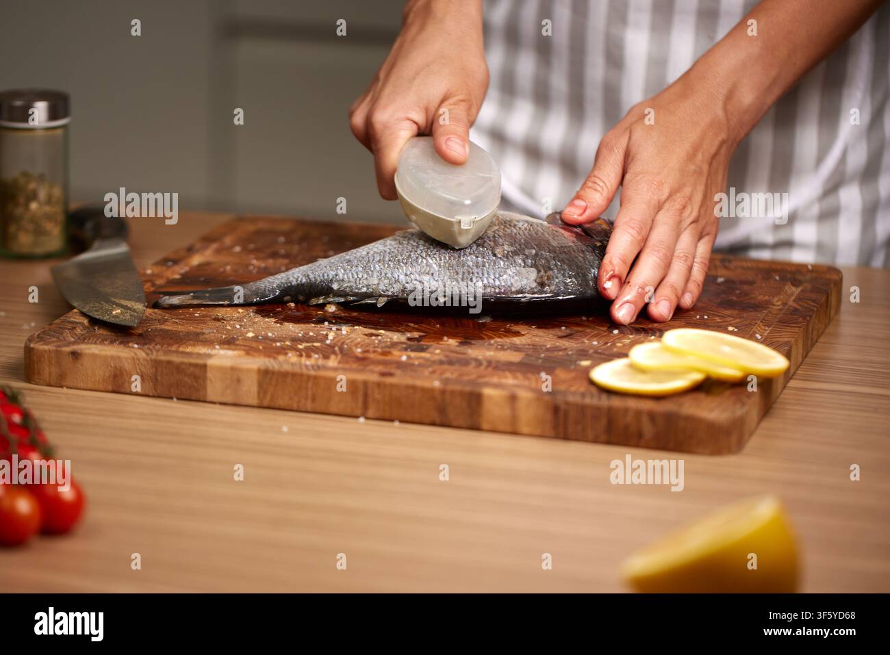 Chef descaling fresh sea bream in kitchen Stock Photo