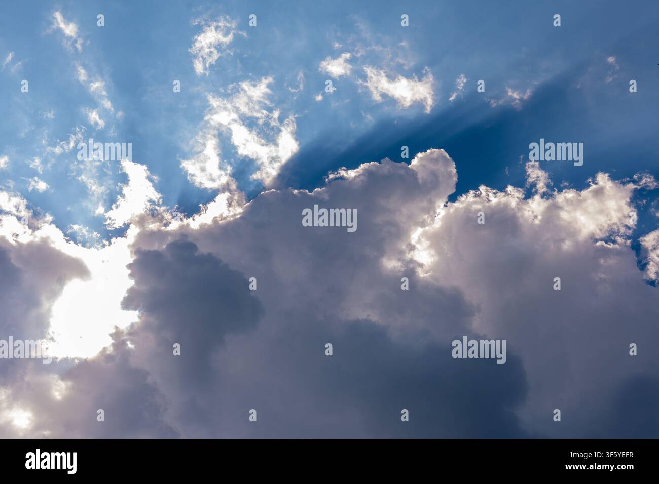 Bright sunlight shines from behind large dramatic clouds against a deep blue sky. Stock Photo
